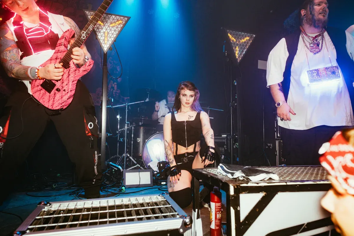 Taenzerin sitzt auf Buehnenkante umgeben von Band und blauen Lichtern